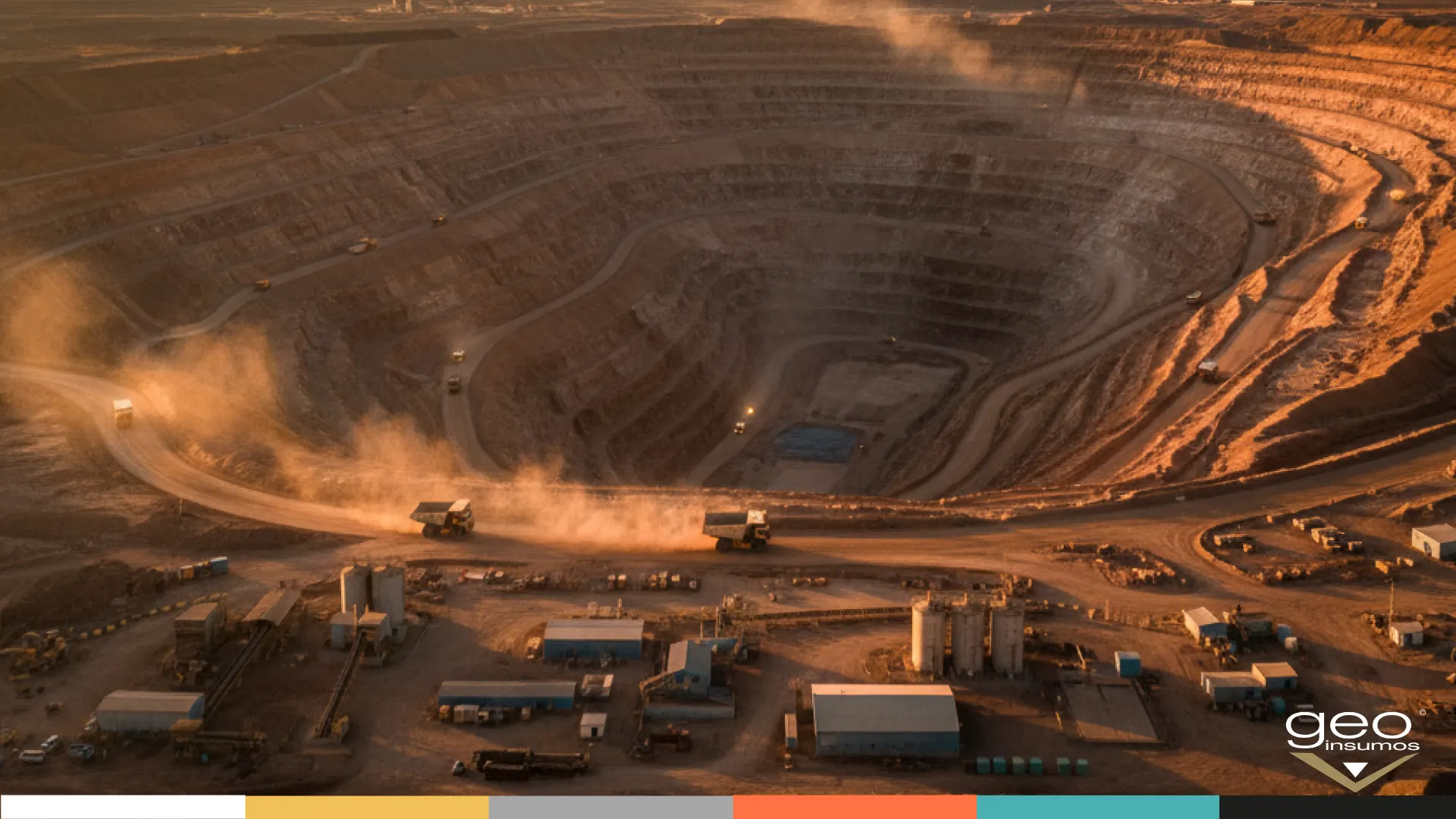 Rajo abierto al atardecer con camiones de extracción en circulación y planta de proceso en operación.
